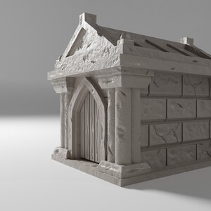 May include: A small, grey stone mausoleum with a single arched doorway and a decorative roof. The mausoleum is made of rough-hewn stone and has a weathered appearance.