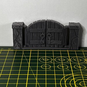 May include: A gray, wooden gate with a chain and padlock. The gate is closed and has a slightly arched top. The gate is sitting on a green cutting mat.