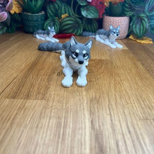Peut inclure: Trois figurines de chien husky gris et blanc, deux sont couch&eacute;es et une est assise. Les figurines sont sur une surface en bois.