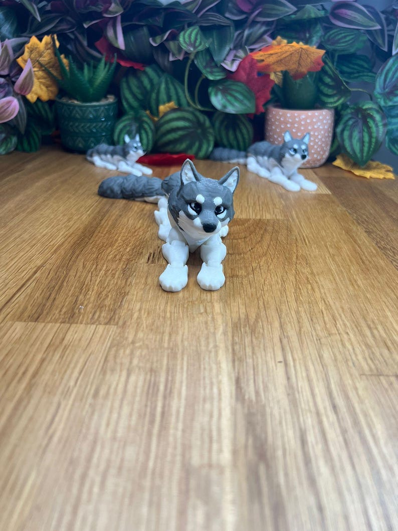 Peut inclure: Trois figurines de chien husky gris et blanc, deux sont couch&eacute;es et une est assise. Les figurines sont sur une surface en bois.