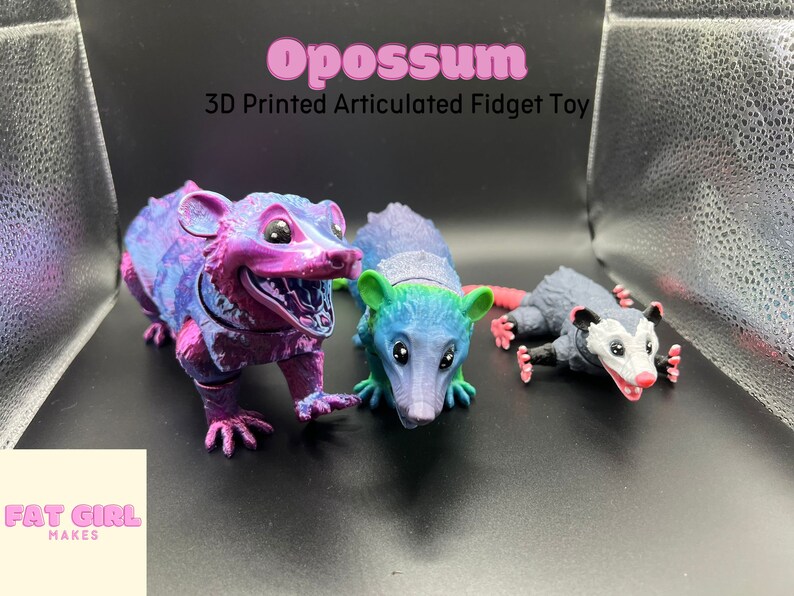 May include: Three 3D printed articulated opossum fidget toys. The opossums are in different colors and poses. The text "Opossum 3D Printed Articulated Fidget Toy" is above the toys. The text "Fat Girl Makes" is below the toys.