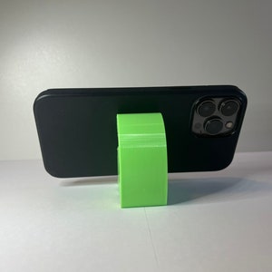 May include: A black smartphone with a green phone stand. The phone is in a black case and the stand is made of plastic.
