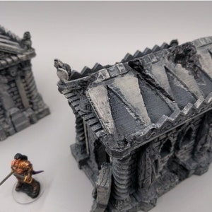 May include: Two detailed, gray, stone miniature buildings with a weathered, aged look. The buildings are in the style of a mausoleum or crypt. One building has a broken roof.