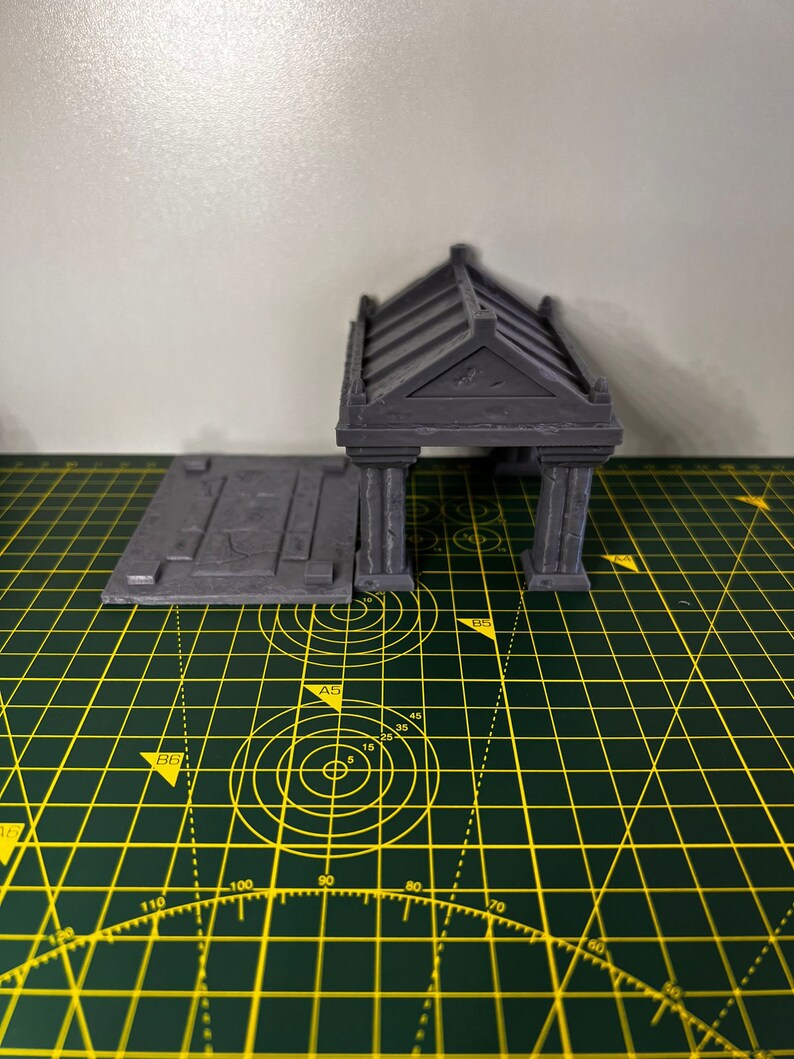 May include: A grey 3D printed model of a small building with a flat roof and a rectangular base. The building has a series of columns and a decorative roof.