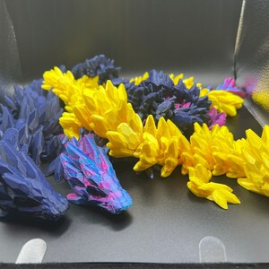 May include: Three 3D printed dragon figurines. One is blue, one is yellow, and one is purple and blue.