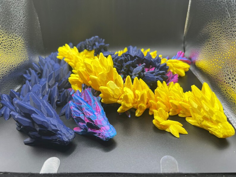 May include: Three 3D printed dragon figurines. One is blue, one is yellow, and one is purple and blue.