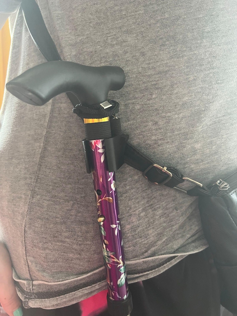 May include: A purple and white floral patterned walking stick with a black handle is attached to a black strap and worn across the body.