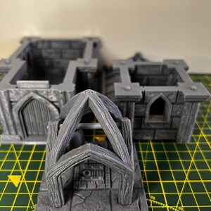 May include: A gray 3D printed miniature of a stone archway with a wooden frame. The archway is set on a square base with a stone floor.