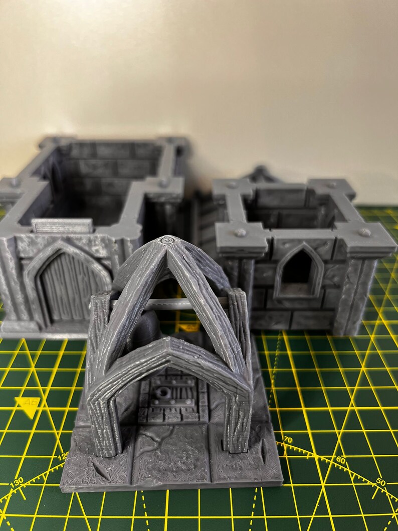 May include: A gray 3D printed miniature of a stone archway with a wooden frame. The archway is set on a square base with a stone floor.