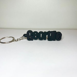 Op de afbeelding: Zwarte plastic sleutelhanger met de naam "George" in vetgedrukte letters.