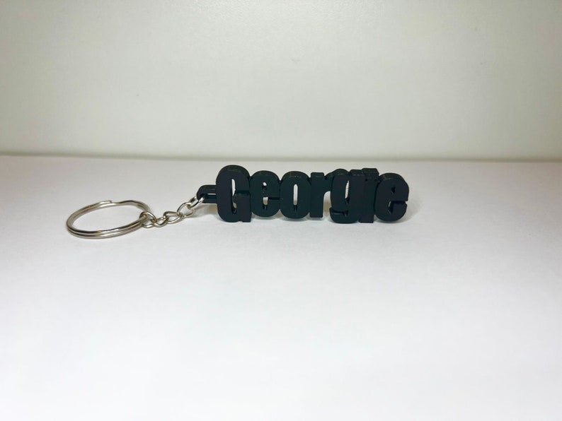 Op de afbeelding: Zwarte plastic sleutelhanger met de naam "George" in vetgedrukte letters.
