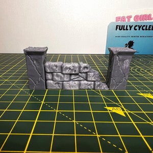 May include: A gray stone wall miniature with a broken section, perfect for tabletop gaming or miniature painting. The wall is made of two pillars and a connecting section with a rough, textured surface.