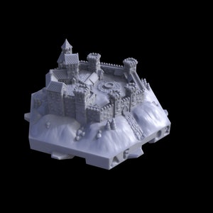 Op de afbeelding: Een gedetailleerd, grijs miniatuur kasteelmodel met meerdere torens, muren en een centrale binnenplaats. Het kasteel staat op een verhoogd platform, wat duidt op een versterkte structuur. Het model staat tegen een zwarte achtergrond.