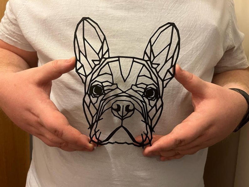 May include: A black paper cut-out of a French bulldog's head, with geometric shapes forming the outline of the dog's face.