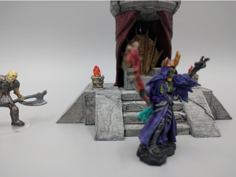 May include: A miniature figure of a skeletal figure wearing a purple robe and a crown, holding a staff. The figure is standing on a stone platform with steps leading up to a throne with a red curtain.