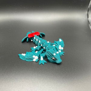May include: Teal blue 3D printed dragon figurine with white accents and a red stripe on its back. The dragon has a small, detailed face with black eyes.