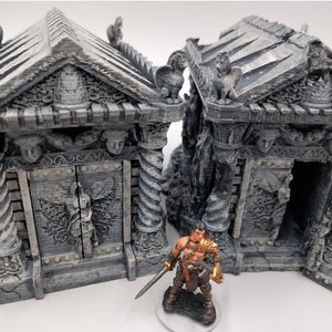 May include: Two detailed grey stone miniature buildings with intricate carvings and a small warrior figurine standing in front of them.