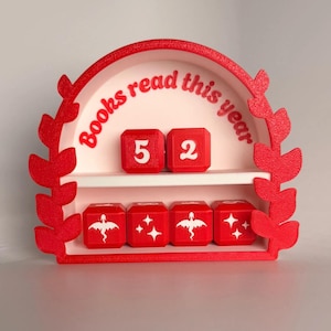 May include: A red 3D-printed book counter with the text "Books read this year." The counter displays the number "52" on two red dice. Below, four red cubes feature a dragon and stars.
