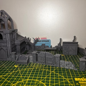 May include: A 3D printed miniature set of a gothic church, a gate, a wall, and a small building with a chimney. The set is painted in a gray color and is made of plastic.
