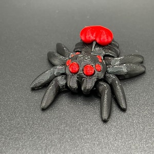 May include: A black 3D printed spider with red eyes and a red abdomen. The spider is posed with its legs spread out.