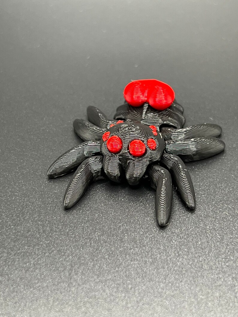May include: A black 3D printed spider with red eyes and a red abdomen. The spider is posed with its legs spread out.