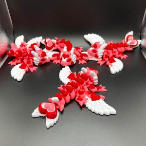 Puede incluir: Cinco criaturas aladas de color rosa y rojo con corazones en sus cuerpos. Las alas son blancas con un borde festoneado. Las criaturas est&aacute;n dispuestas en un grupo sobre un fondo negro.