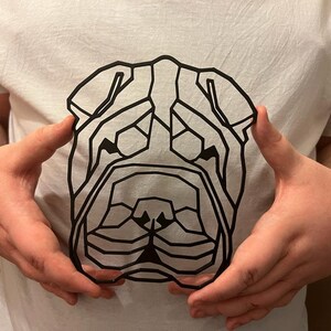 K&ouml;nnte beinhalten: Ein wei&szlig;es T-Shirt mit einem geometrischen Schwarz-Wei&szlig;-Design eines Shar-Pei-Hunde-Kopfes.