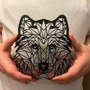 May include: A black geometric wolf head cutout, held in the hands of a person.