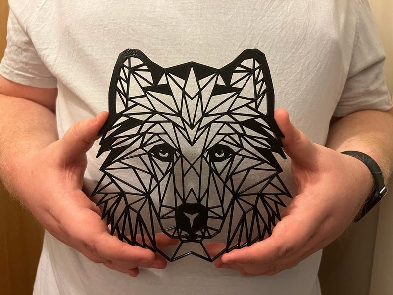 May include: A black geometric wolf head cutout, held in the hands of a person.