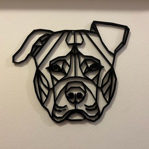 May include: Black and white geometric design of a dog's head, resembling a pit bull terrier, mounted on a white wall.