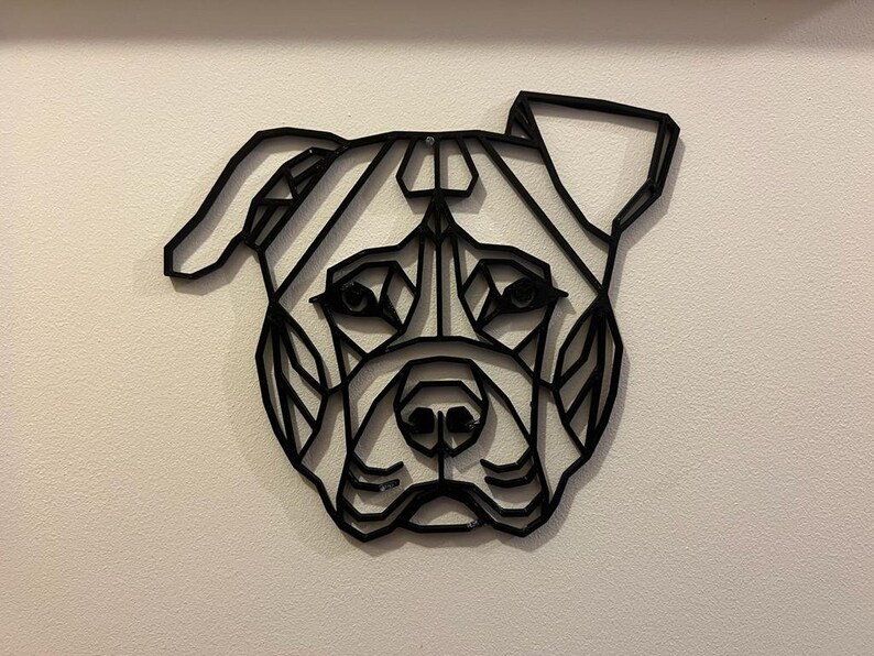 May include: Black and white geometric design of a dog's head, resembling a pit bull terrier, mounted on a white wall.