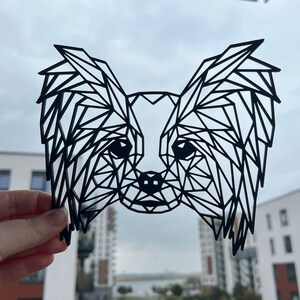 Puede incluir: Corte de papel geom&eacute;trico negro de un perro papillon. Las orejas del perro son grandes y ca&iacute;das, y su cara est&aacute; detallada con una nariz peque&ntilde;a y ojos grandes.