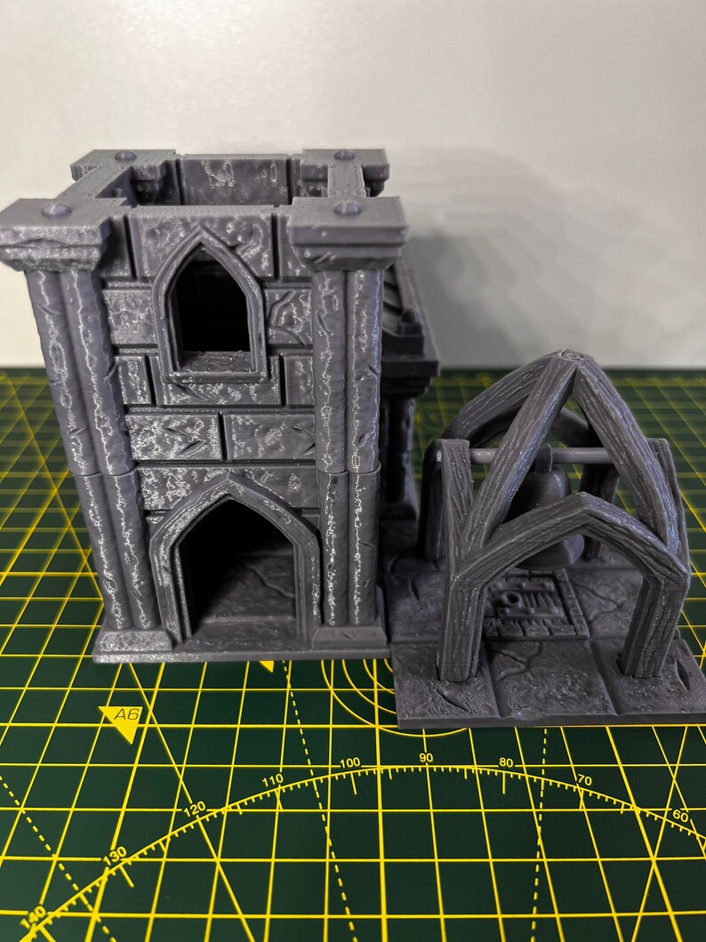 May include: A gray 3D printed miniature tower with a bell tower attached. The tower has a window and an arched doorway. The bell tower has a bell inside.