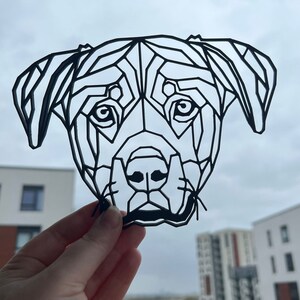 May include: Black and white geometric paper cut-out of a dog's head. The dog has a short, flat nose and floppy ears.