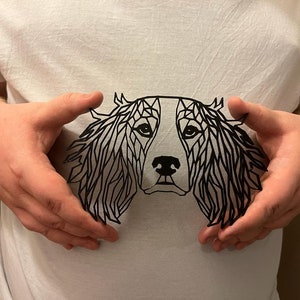 May include: A black paper cut-out of a dog's head in a geometric style. The dog has floppy ears and a long snout.