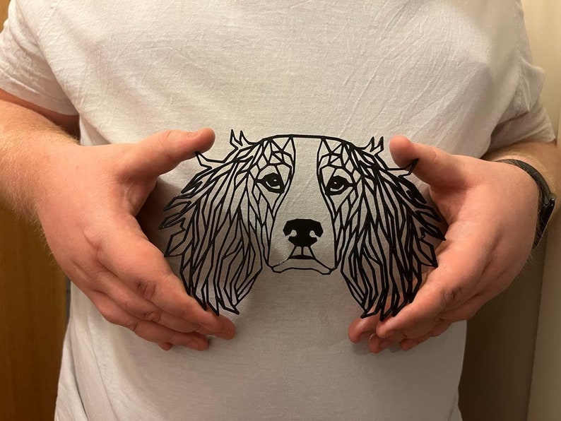 May include: A black paper cut-out of a dog's head in a geometric style. The dog has floppy ears and a long snout.