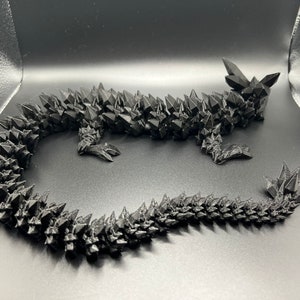 May include: A black, 3D printed dragon sculpture with a spiky, textured surface. The dragon is curled up with its tail wrapped around its body.