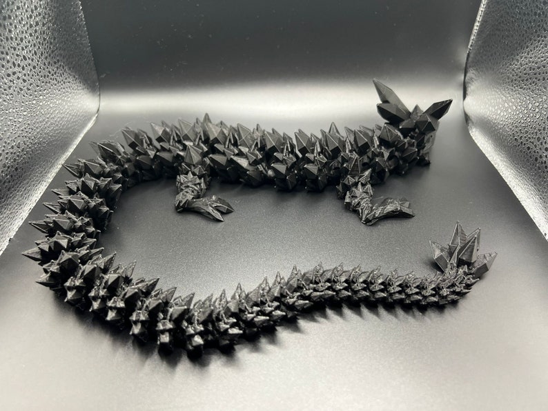 May include: A black, 3D printed dragon sculpture with a spiky, textured surface. The dragon is curled up with its tail wrapped around its body.