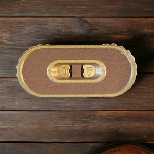 Pode incluir: Um objeto decorativo de madeira com acabamento marrom e dourado. O objeto apresenta os números "07" na frente e tem uma superfície texturizada.