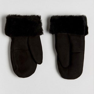 May include: A pair of black faux fur lined mittens. The mittens are made of a soft, suede-like material and have a fold-over cuff.