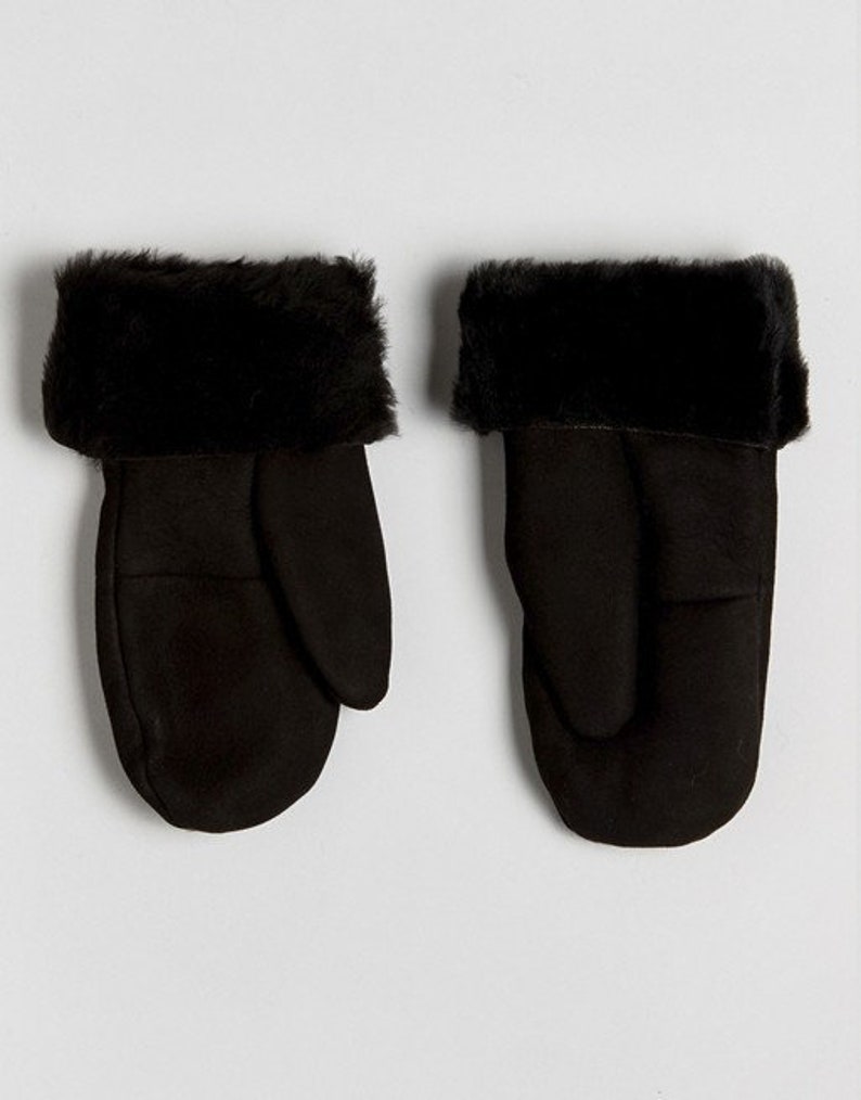 May include: A pair of black faux fur lined mittens. The mittens are made of a soft, suede-like material and have a fold-over cuff.