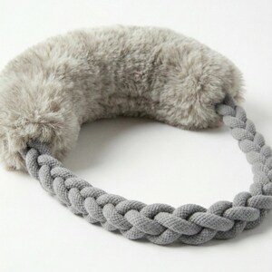 Puede incluir: Un calentador de orejas de piel sintética gris con una diadema trenzada gris. La cubierta de la oreja es un material suave y esponjoso. La diadema está hecha de una tela gruesa y tejida. El calentador de orejas está diseñado para mantener las orejas calientes en climas fríos.