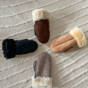 May include: Four pairs of brown, black, and beige suede mittens with faux fur trim. The mittens are laid out on a white textured surface.