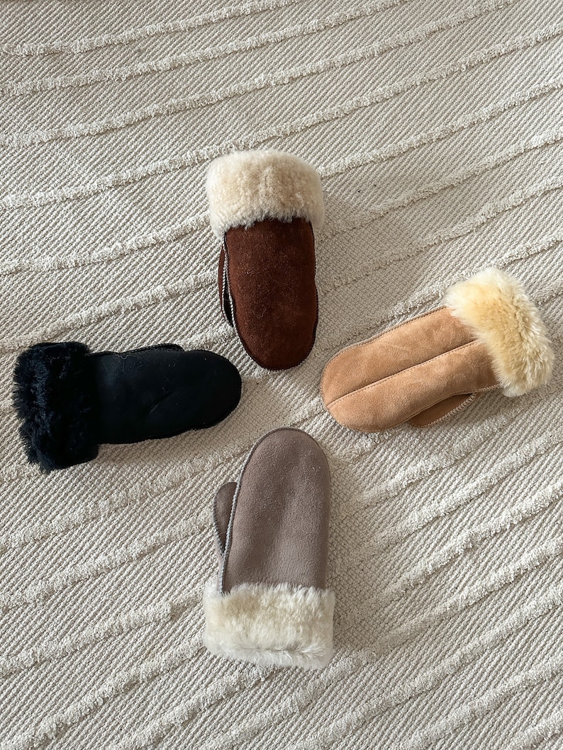 May include: Four pairs of brown, black, and beige suede mittens with faux fur trim. The mittens are laid out on a white textured surface.