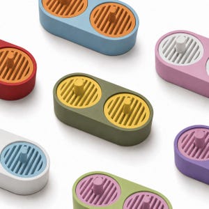 May include: A collection of oval-shaped, dual-compartment organizers in various colors, including light blue, red, olive green, pink, white, and purple. Each unit features two circular, slatted inserts with a central post for holding items.