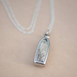 May include: A silver chain necklace with a pendant featuring a clear glass vial filled with white fibers.