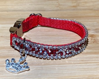 Könnte beinhalten: Rotes Haustierhalsband mit silberfarbenen Strasssteinen und einem silbernen Kronenanhänger. Das Halsband hat eine silberne Schnalle und ist etwa 1,3 cm breit. Für kleine Haustiere.