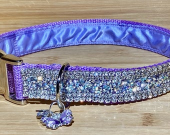 Könnte beinhalten: Ein lila Hundehalsband mit einer silbernen Schnalle und einem silbernen Schmetterlingsanhänger. Das Halsband ist mit Reihen aus klaren Strasssteinen verziert.
