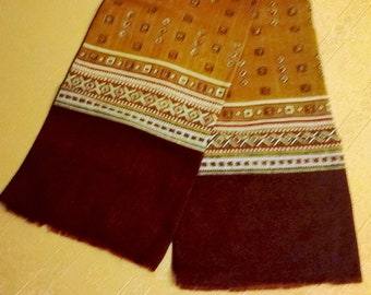 May include: A rectangular scarf with a patterned design. The scarf features a maroon border and a central section with a repeating square pattern in shades of gold and brown. The design includes geometric and linear elements.