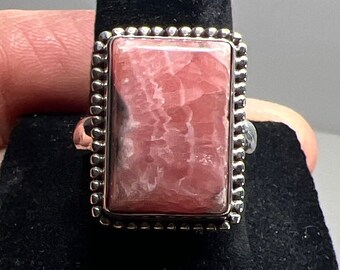 May include: A silver ring with a pink and white rectangular gemstone set in a beaded border.